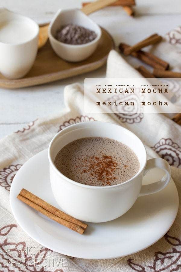 a cup of mexican mocha next to cinnamon sticks