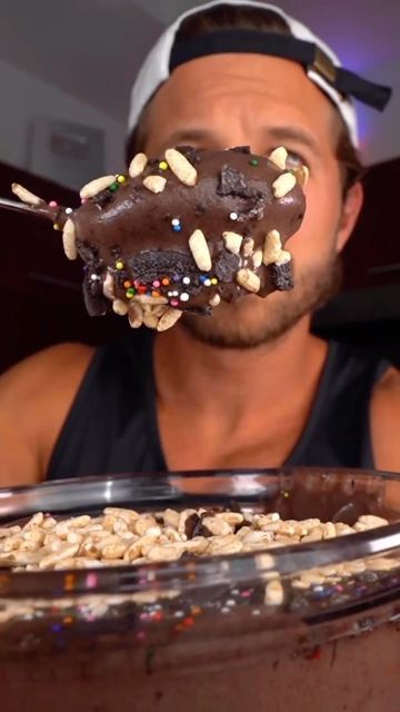 a man eating a chocolate donut with sprinkles on top of it