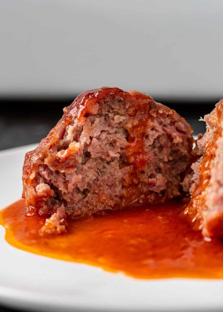 two meatballs covered in marinara sauce on a white plate with a black background