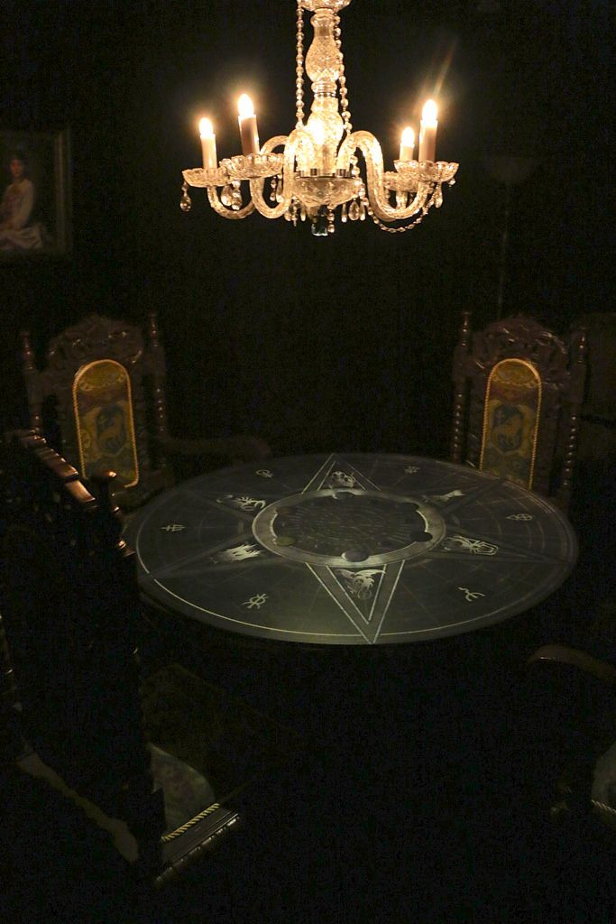 a chandelier hanging from the ceiling in a dark room with chairs around it