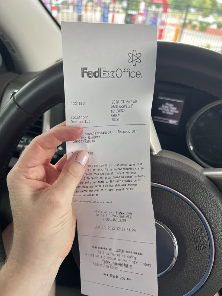 a person holding up a receipt in their hand next to the steering wheel of a car