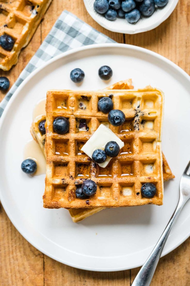 waffles with butter and blueberries on a white plate next to silverware