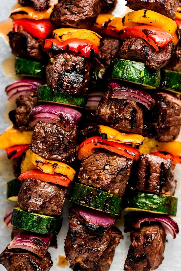 skewered steaks with peppers and onions on a sheet of parchment paper