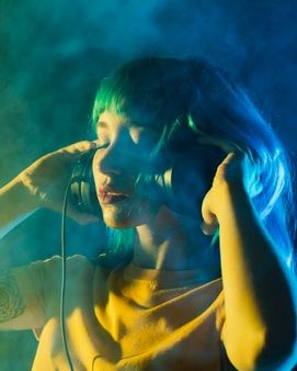 a woman with blue hair is holding a microphone and listening to music on her headphones