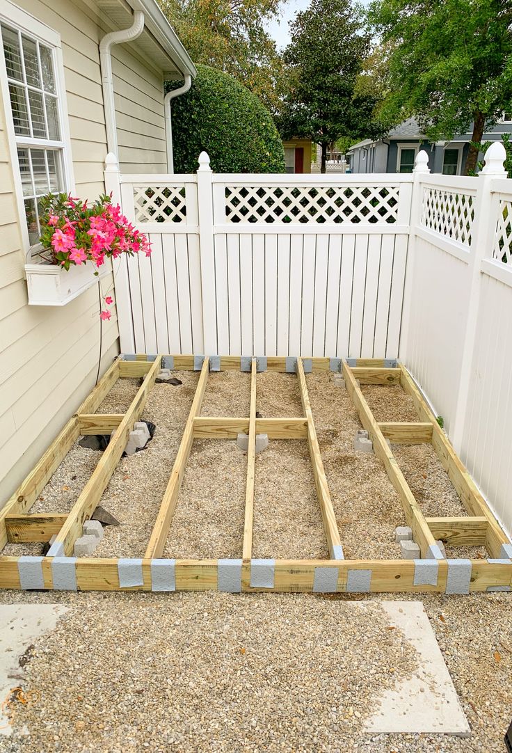 an unfinished bed frame in front of a white fence and flower potted planter