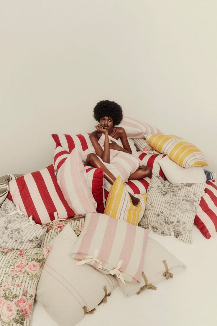 a woman sitting on top of a pile of pillows with her face in her hands