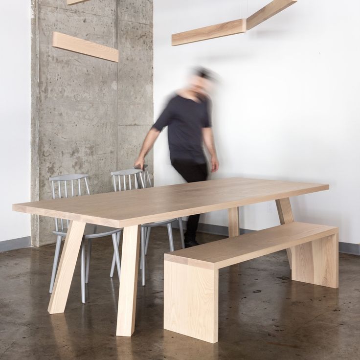 a person standing in front of a wooden table with two chairs and a bench underneath it