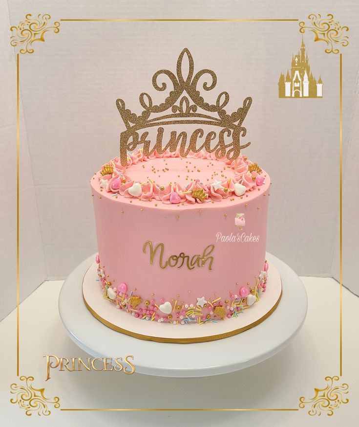 a princess cake with pink frosting and gold lettering on top, sitting on a white plate