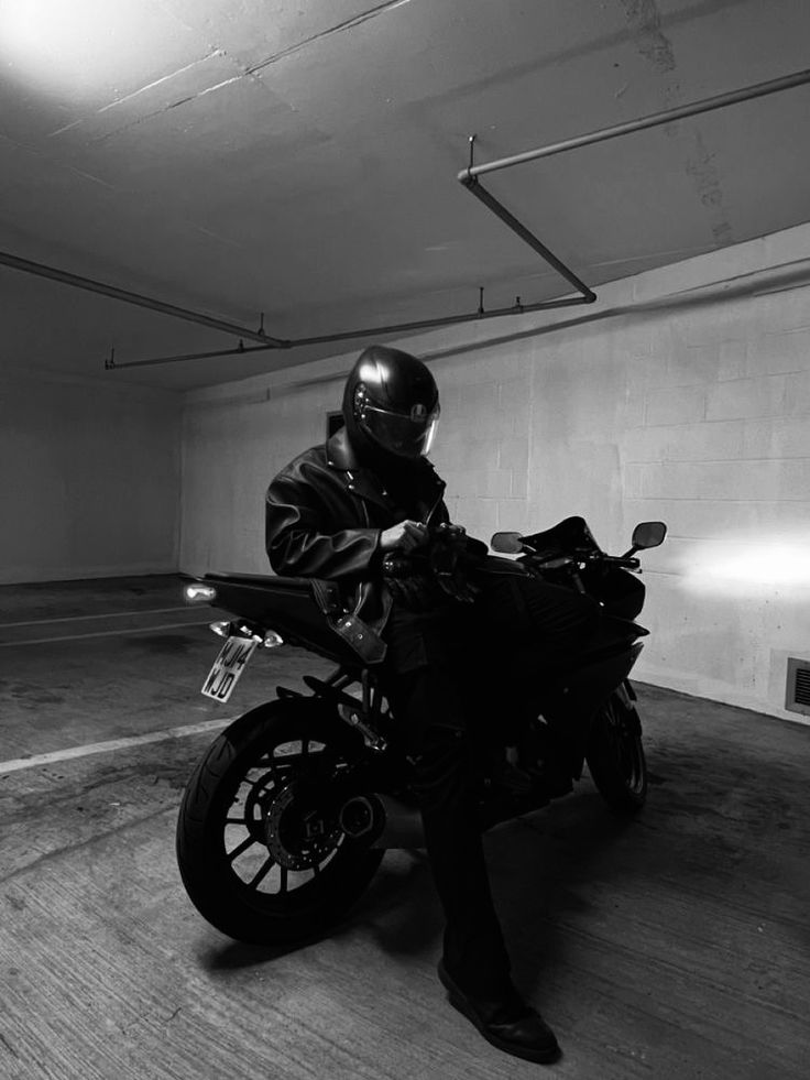 a man sitting on a motorcycle in an empty parking garage, wearing a helmet and protective gear