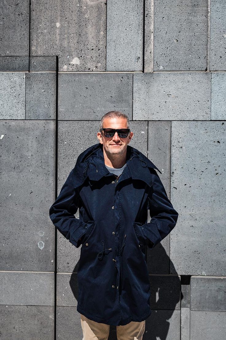 a man standing in front of a wall with his hands on his hips wearing sunglasses