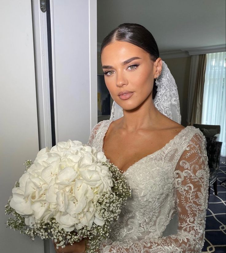 a woman in a wedding dress holding a bouquet of flowers and looking at the camera