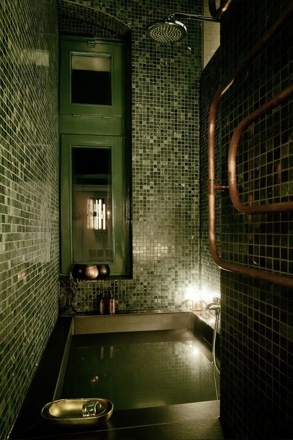 a dimly lit bathroom with green and brown tiles on the walls, floor and tub