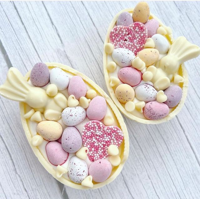 two easter eggs decorated with candy and sprinkles on a white wooden surface