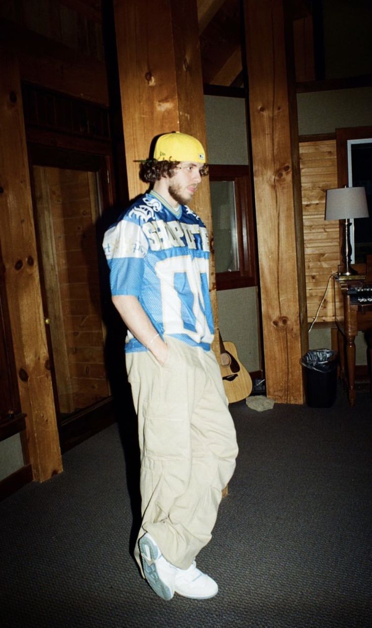 a young man in a blue and white football jersey standing next to a wall with wood paneling