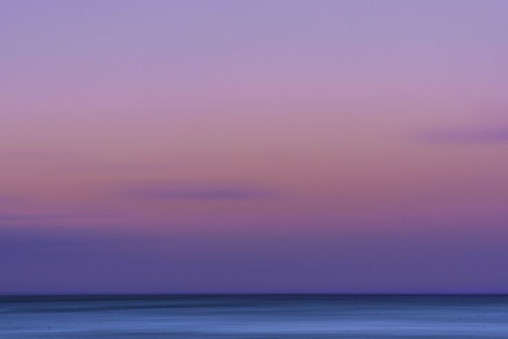 an airplane is flying over the ocean at sunset or dawn with purple and blue hues