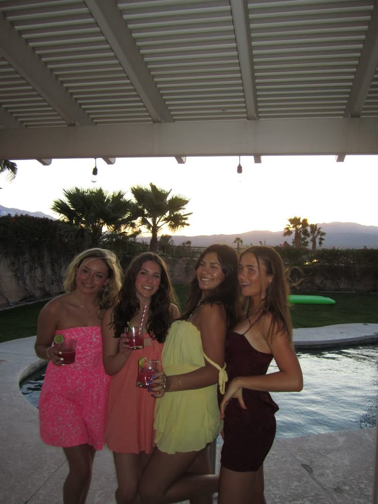 four beautiful women standing next to each other in front of a pool at night time