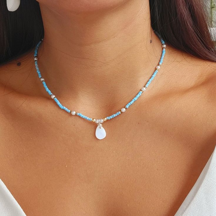 a woman wearing a blue and white necklace with a tear shaped pendant on it's neck