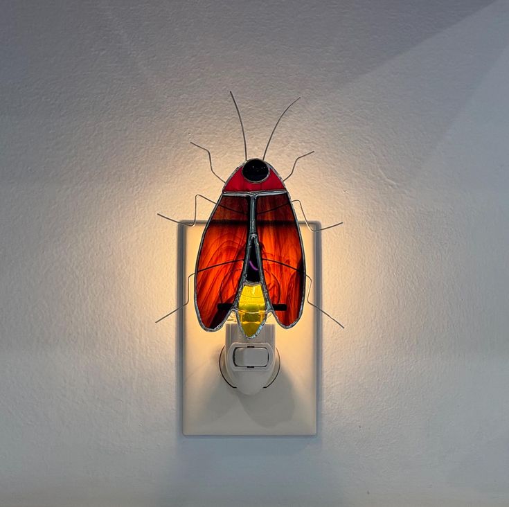 a red and black insect sitting on top of a white light switch cover in a room