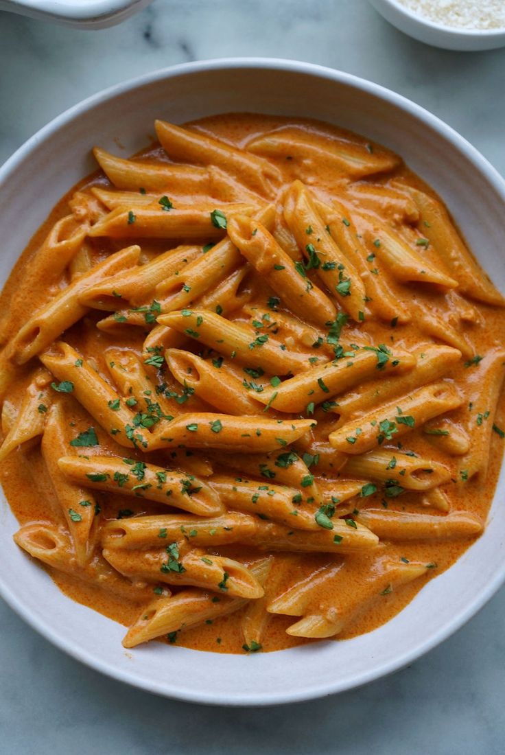 a white bowl filled with pasta and sauce on top of a marble table next to two bowls