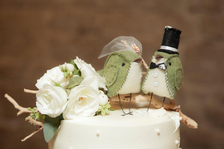 two birds are perched on top of a wedding cake with white flowers and greenery