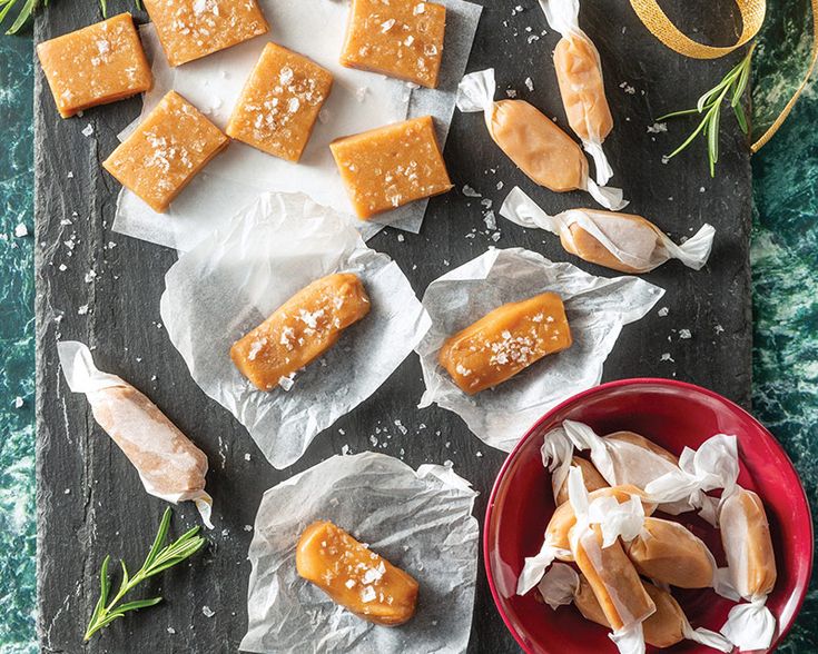 several pieces of caramel cheese on wax paper next to a red bowl and green sprig