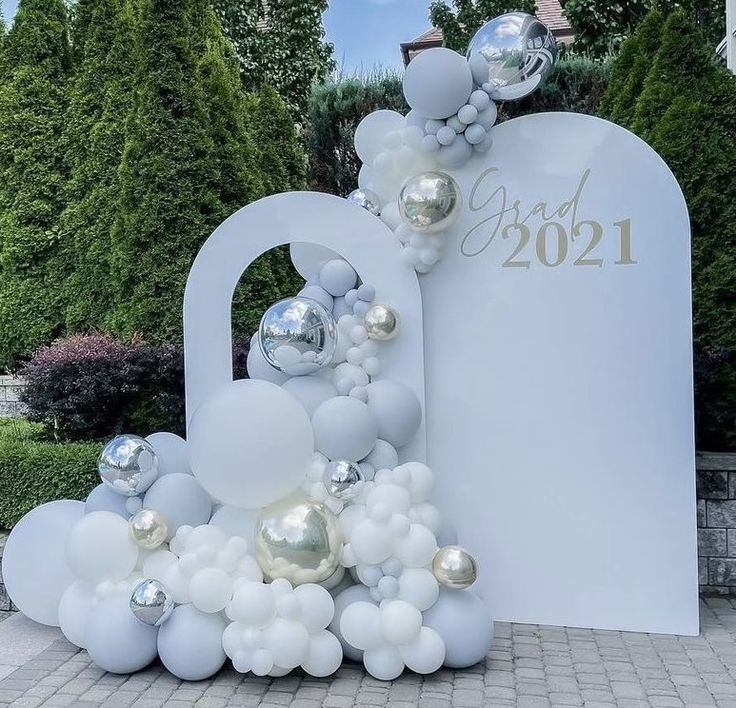 a large balloon arch with silver and white balloons on it in front of a sign