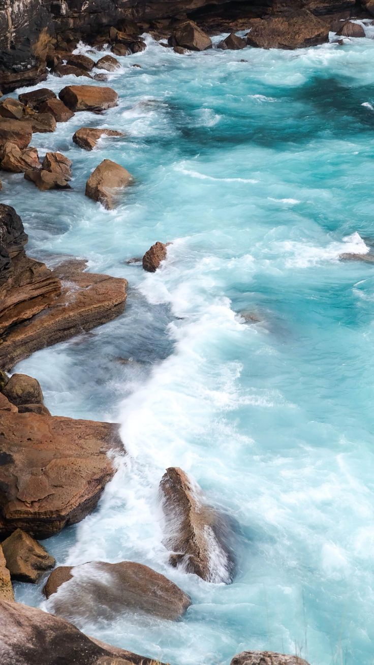 the water is blue and foamy as it flows through some rocky coastlines with large rocks