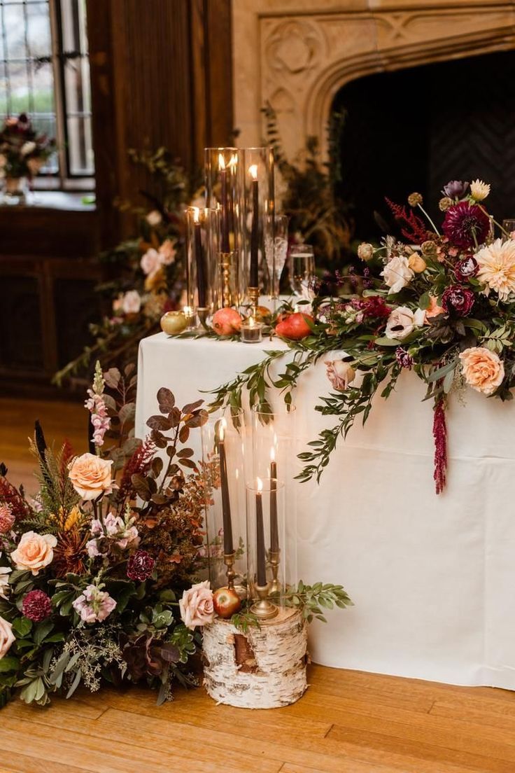 an arrangement of flowers and candles on a white table cloth in front of a fireplace