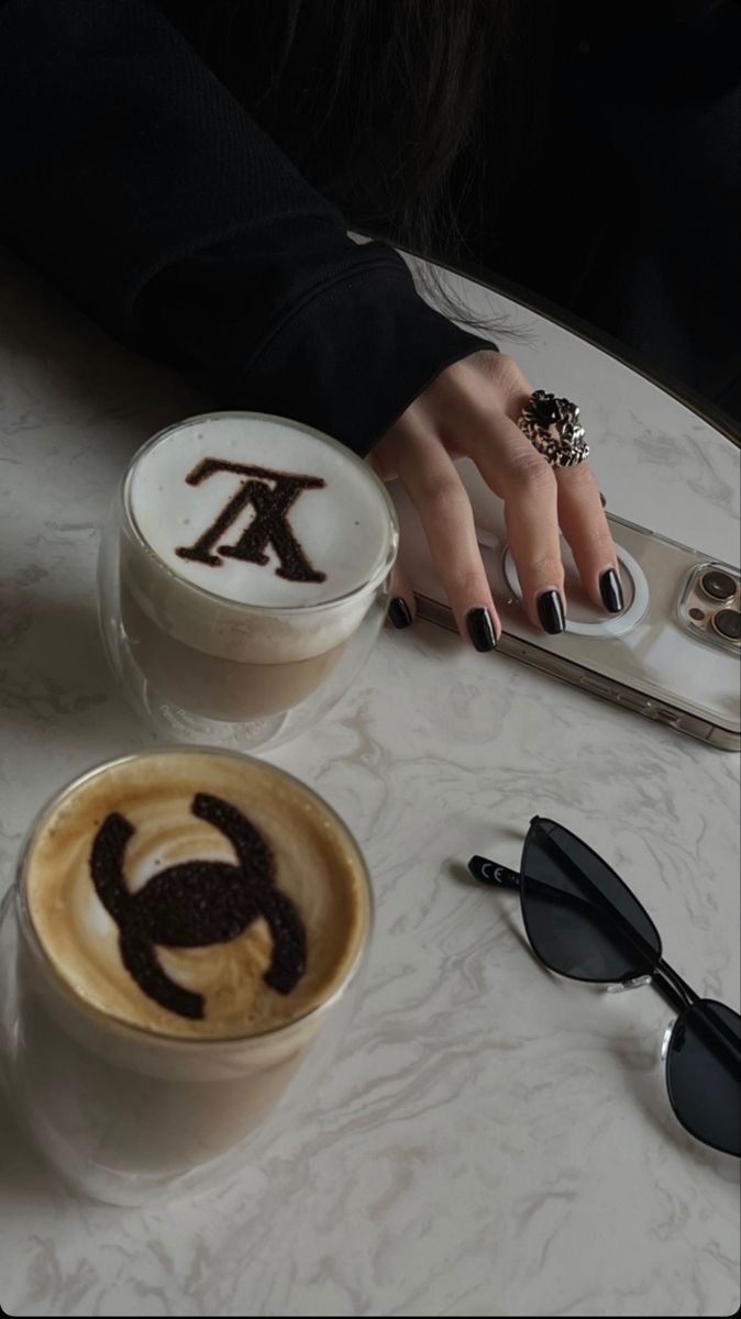 a woman's hand with black nail polish on her nails next to two cups of coffee