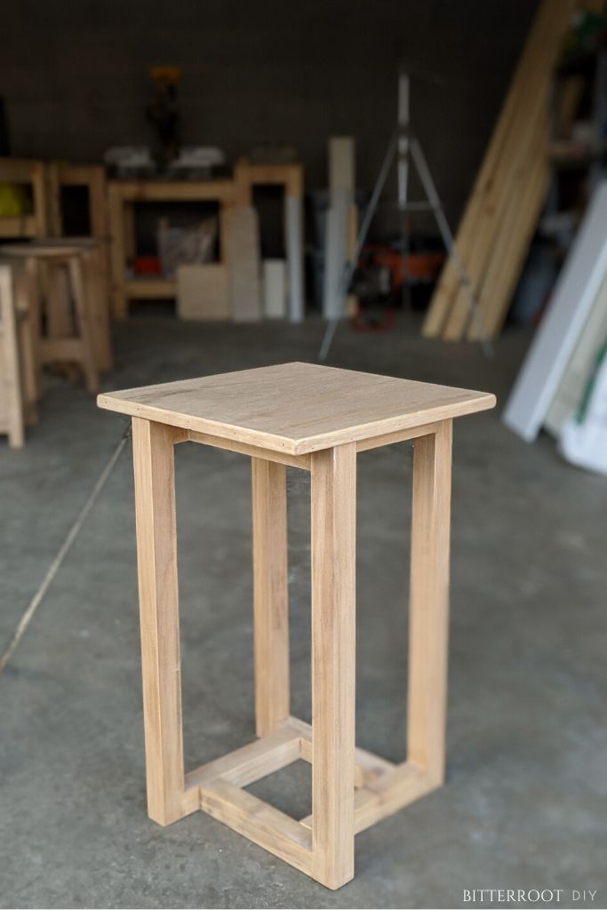 a small wooden table sitting on top of a cement floor in a room filled with woodworking tools