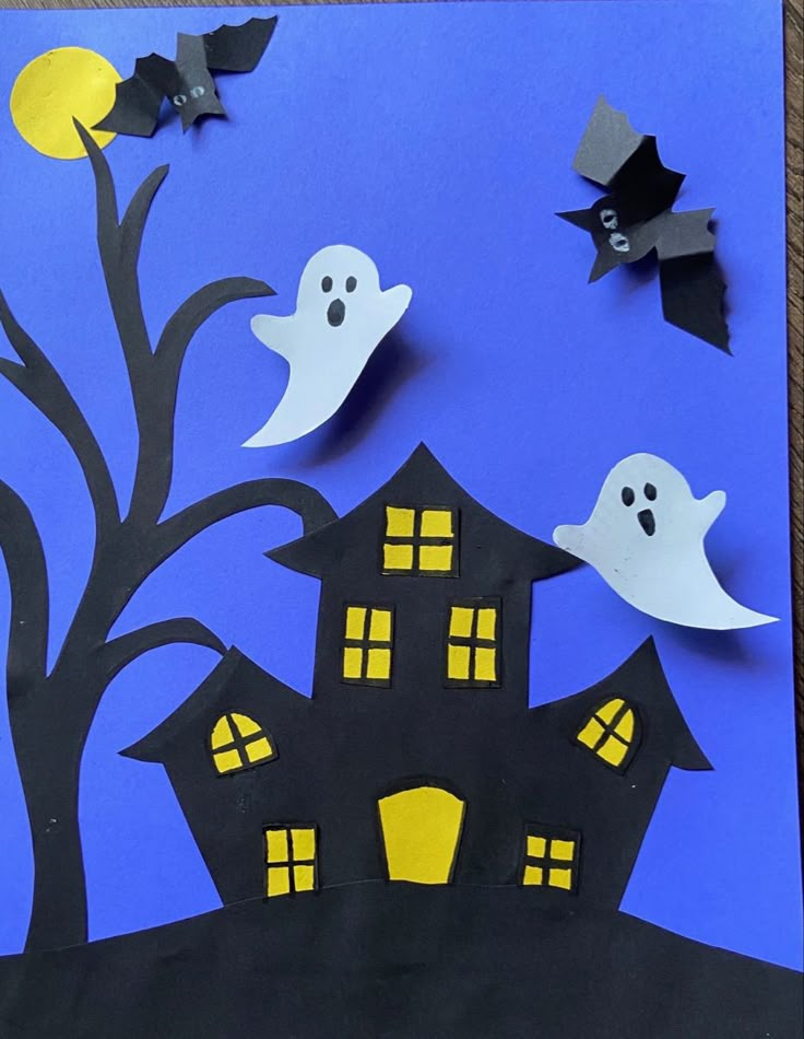 paper cut out of the shape of a house with bats flying over it and two ghost houses