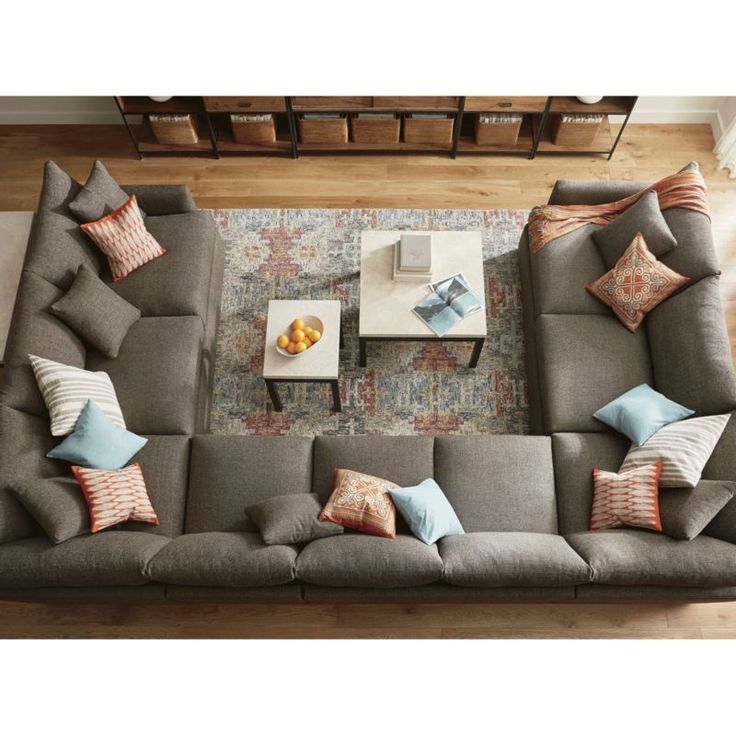 an overhead view of a living room with grey couches and colorful pillows on the coffee table