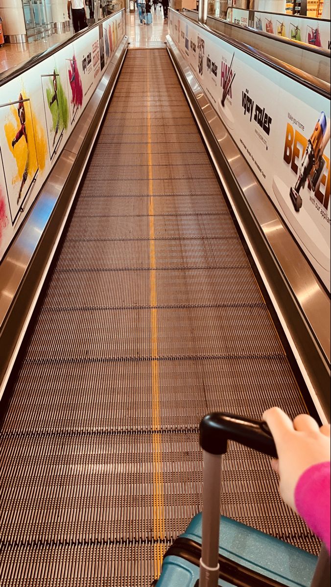 a person pushing a luggage cart down an escalator in a shopping center with advertisements on the wall