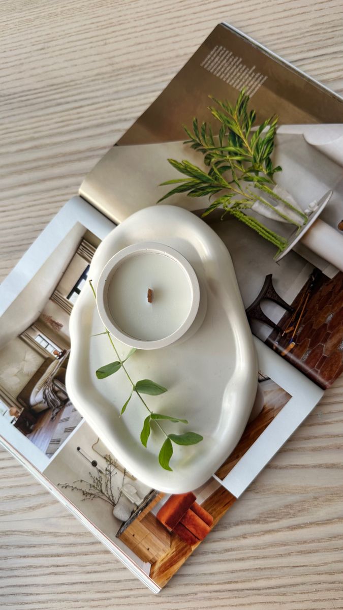 a white candle holder sitting on top of a wooden table next to a magazine and some plants