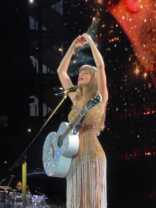 a woman in a dress holding a guitar and singing on stage with fireworks behind her