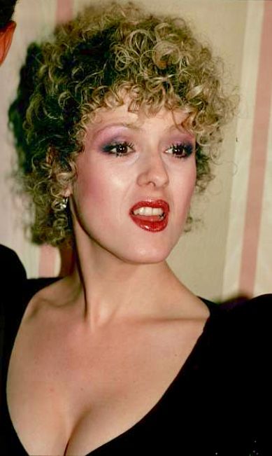 a close up of a person with curly hair and red lipstick wearing a black dress