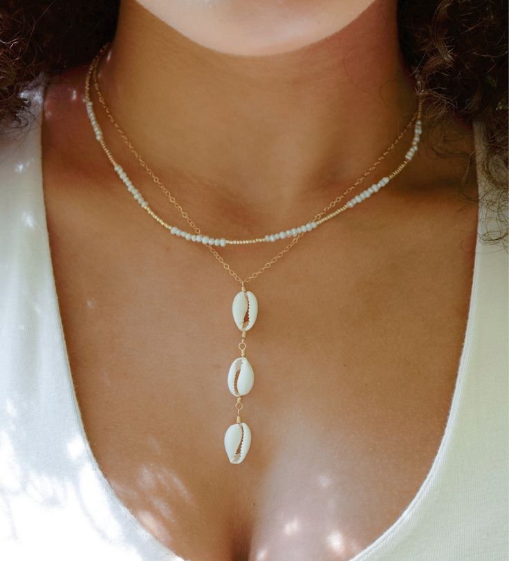 Release your inner beach beauty with our Triple Cowrie Shell Necklace! Handmade with three authentic cream-colored cowrie shells set onto a sterling silver or 14k gold filled chain, this pendant is sure to bring summer vibes to every season! Since each shell is natural, there will be slight variations from one piece to the next. Some shells are longer/wider, while others are more narrow or short. If you have a preference, let us know. Cowrie Shell Meaning: Once used as currency in many cultures Elegant White Cowrie Shell Jewelry, Beachy Gold Beaded Jewelry, Gold Coastal Shell Jewelry, Elegant White Jewelry For Beach Season, Gold Strand Beachy Jewelry, Beachy Gold Strand Jewelry, White Strand Jewelry For Beach Season, White Jewelry For Beach Vacation, White Jewelry For Beach Season Vacation