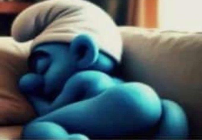 a baby sleeping on top of a couch next to a pillow in the shape of an smurf