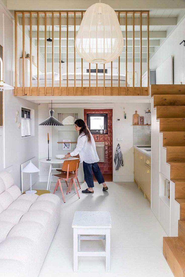 a woman standing in the middle of a living room next to a white couch and stairs