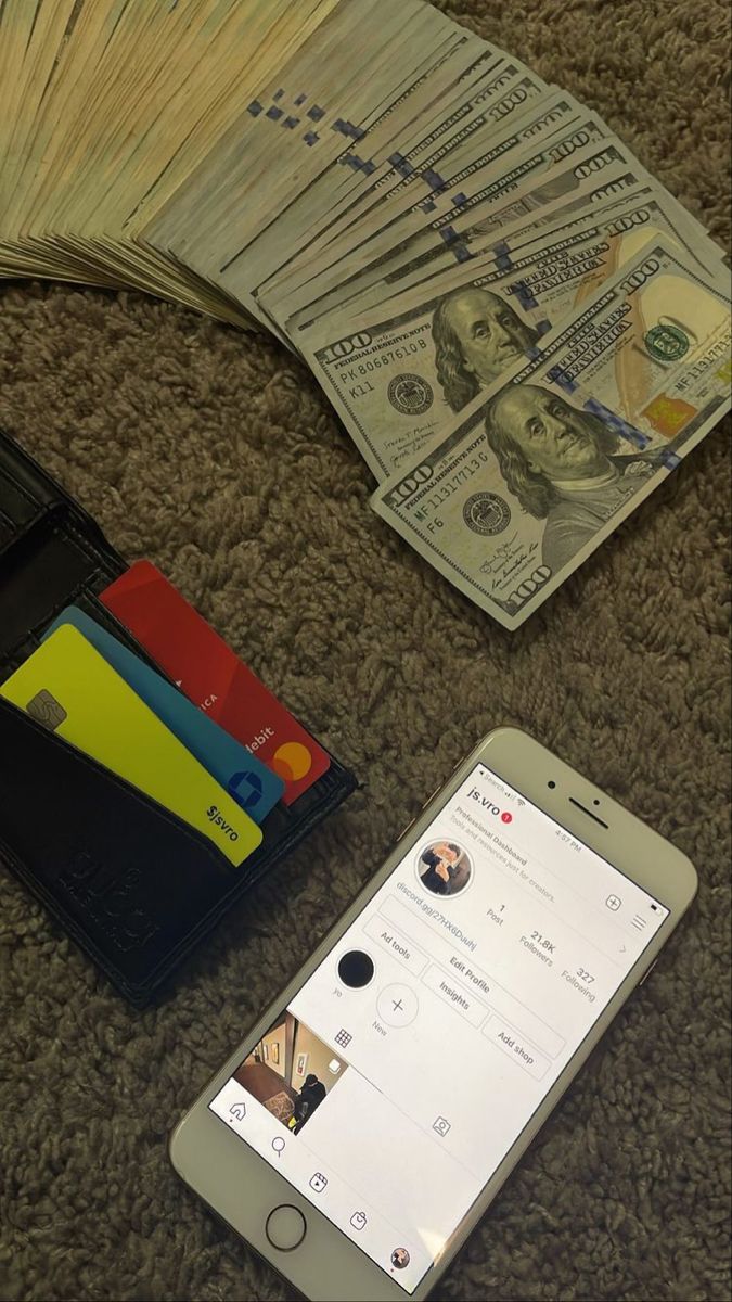 a cell phone sitting next to an open wallet and money on the floor with other items