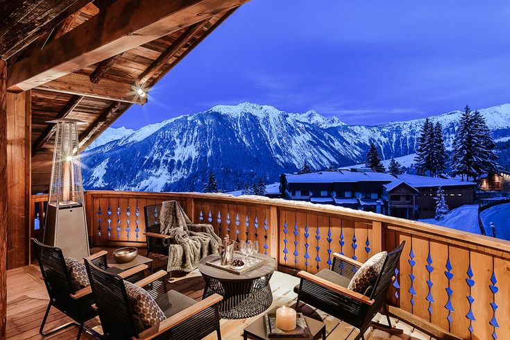 an outdoor deck with chairs and tables overlooking the snow covered mountain range at night time