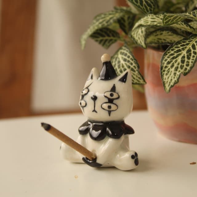 a white cat figurine sitting next to a potted plant on a table