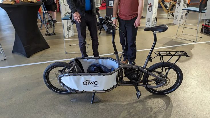 two people standing next to a bike with a basket on the front and back wheels