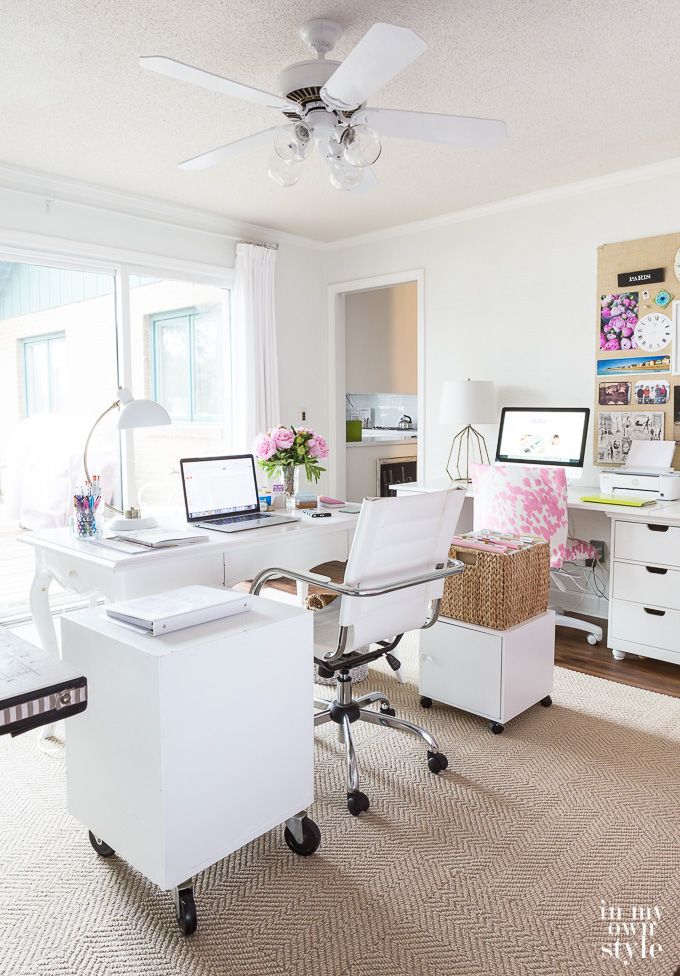 a home office with white furniture and flowers on the desk