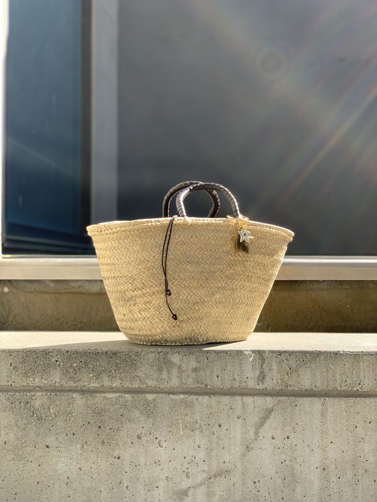 The Brigitte bag is our very modern version of the traditional Panier basket. The basket, handmade by artisans in Spain in palm leaf straw, is covered in a metallic gold mesh, and the short handles coiled in brown leather. It is lined in dark brown cotton fabric, with leather drawstring with metal star charms. The bag is finished with a Cuckoo B keychain featuring a buffalo horn star made in Vietnam, a handmade in Argentina ceramic white star and the Cuckoo B bronze tag. It is inspired on Summer Luxury Gold Straw Bag With Braided Handles, Luxury Handwoven Straw Bag With Top Handle, Luxury Handwoven Top Handle Straw Bag, Luxury Natural Straw Bag For Beach, Luxury Natural Straw Beach Bag, Luxury Gold Straw Bag For Vacation, Chic Straw Bag With Woven Leather For Market, Straw Bag With Woven Leather And Round Handle, Chic Woven Leather Straw Bag For Market