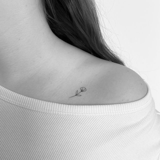 a woman's back shoulder with a single flower tattoo on it