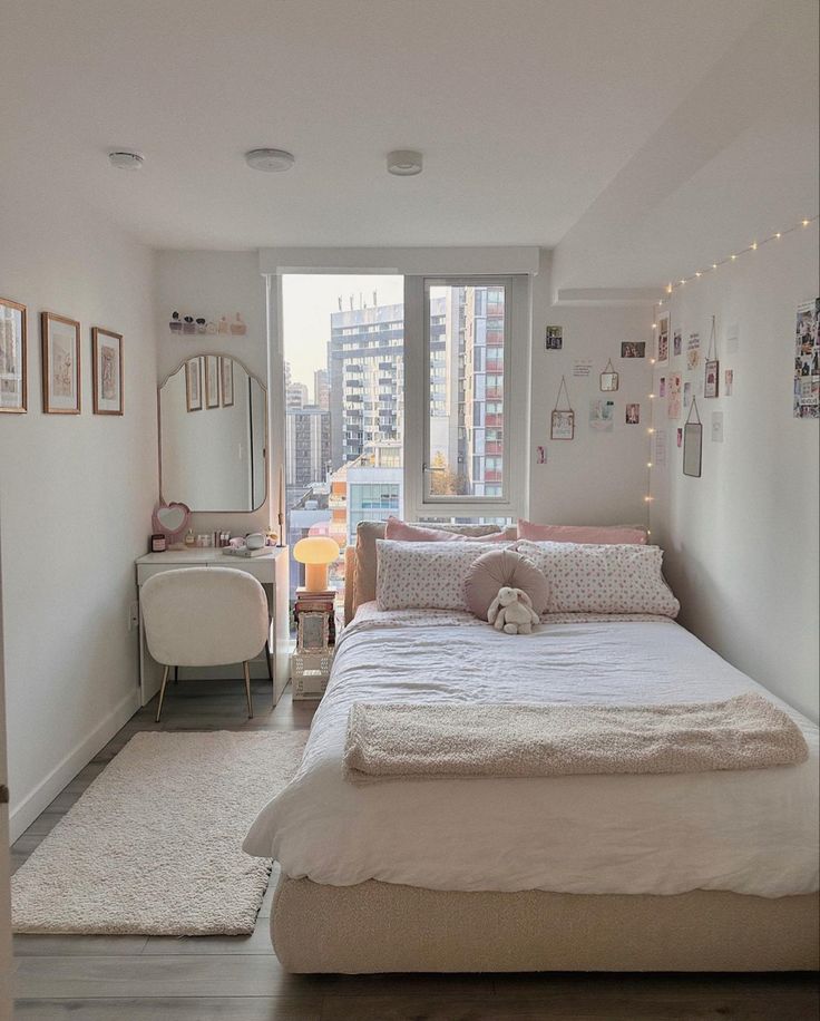 a bedroom with a bed, desk and window in the corner that has city lights on it