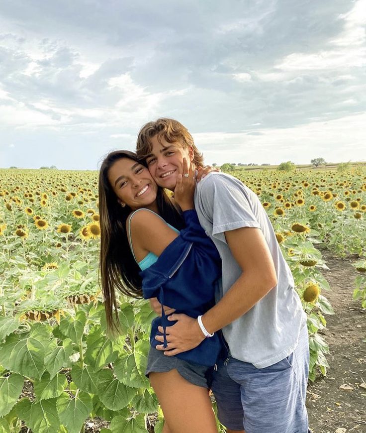 a man and woman standing in front of a field of sunflowers smiling at the camera