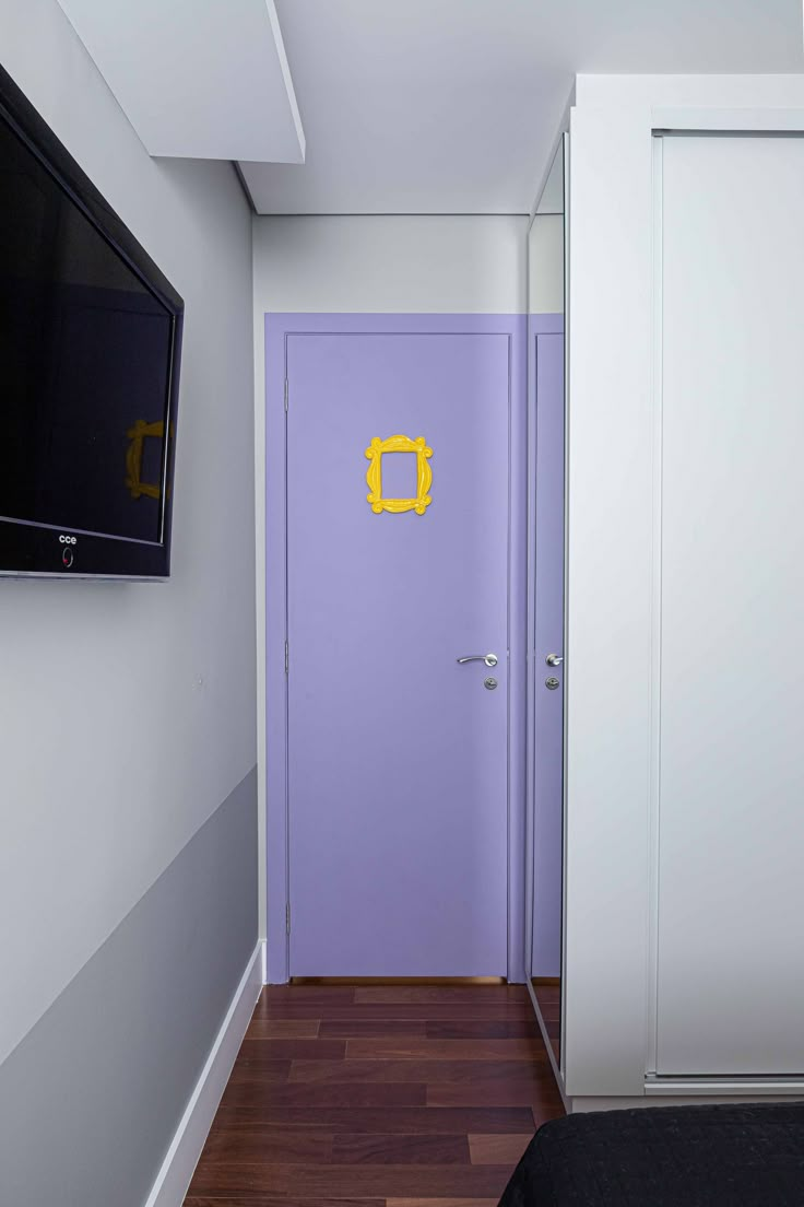 a purple door in a white room next to a bed and flat screen tv on the wall