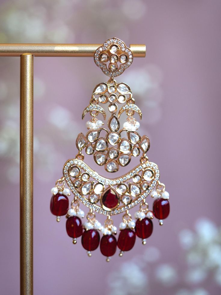 Embrace timeless elegance with our Chashni Chandbali kundan earrings: a masterpiece of traditional craftsmanship and contemporary allure. A stunning piece of unique South Asian jewelry, Chashni is an elegant 21K gold plated chandelier earring adorned with a shimmering Alhambra motif, dangling mini crescents, and lustrous pearls. Chashni's kundan stones are meticulously hand-set by master artisans to create an ethereal array of light that dazzles in every environment. Enhance even your most elegant outfit with the intricate and breathtaking Chashni Chandbali statement earrings.  Materials: 21K gold plating on brass, kundan stones, gemstone beads, pearls Dimensions (L x W): 3.5 x 2.25 inches Weight: 24g (per chandbali) Fusion Style Kundan Chandbali Earrings, Reception Chandbali Chandelier Earrings In Kundan, Fusion Kundan Chandbali Earrings, Fusion Style Kundan Chandbalis With Latkans, Heavy Kundan Fusion Chandbalis, Kundan Temple Jewelry Danglers For Reception, Fusion Style Chandbalis With Cutdana For Reception, Fusion Style Cutdana Chandbalis For Reception, Elegant Chandbalis For Eid Reception